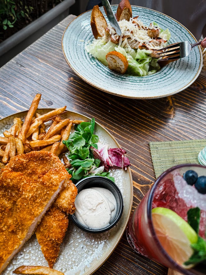 A fried dish with fries, salad, and a refreshing drink on a wooden table.
