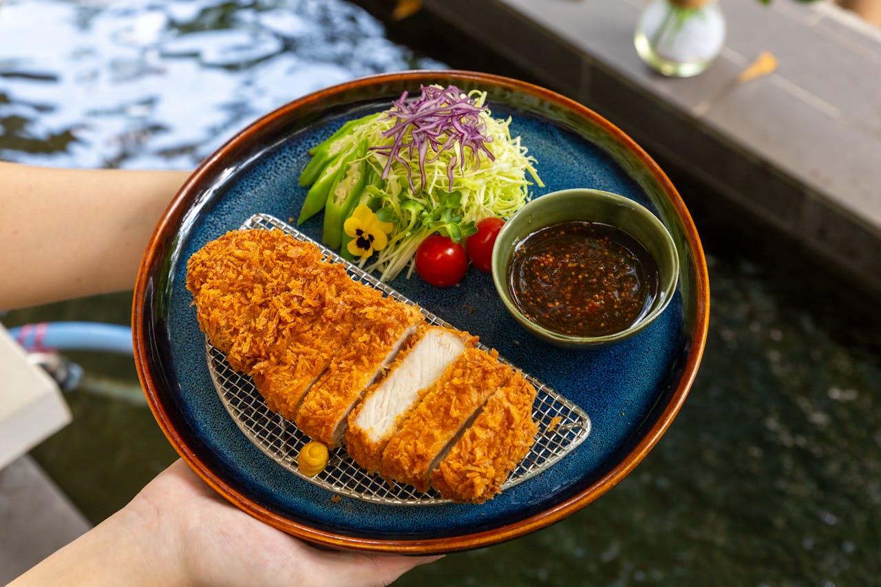 Delicious fried chicken chop with fresh salad and dipping sauce served on a stylish blue plate.