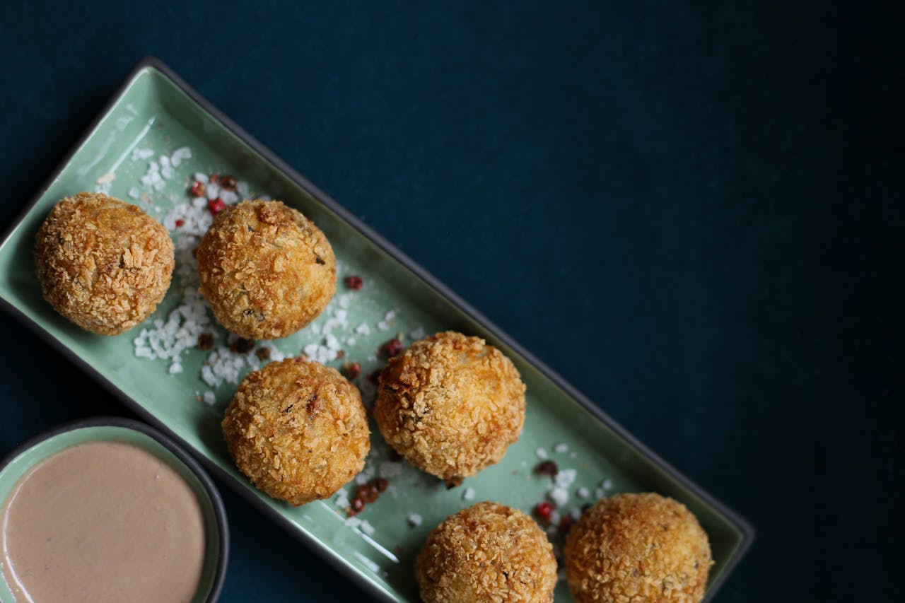 Golden arancini balls on a platter with a side of dipping sauce.