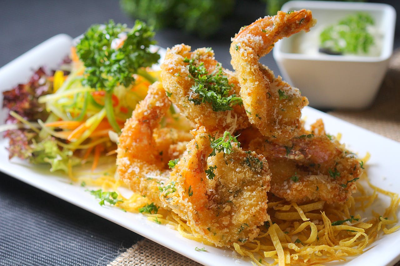 Delicious fried shrimp served with fresh vegetable salad and dipping sauce on a white plate.