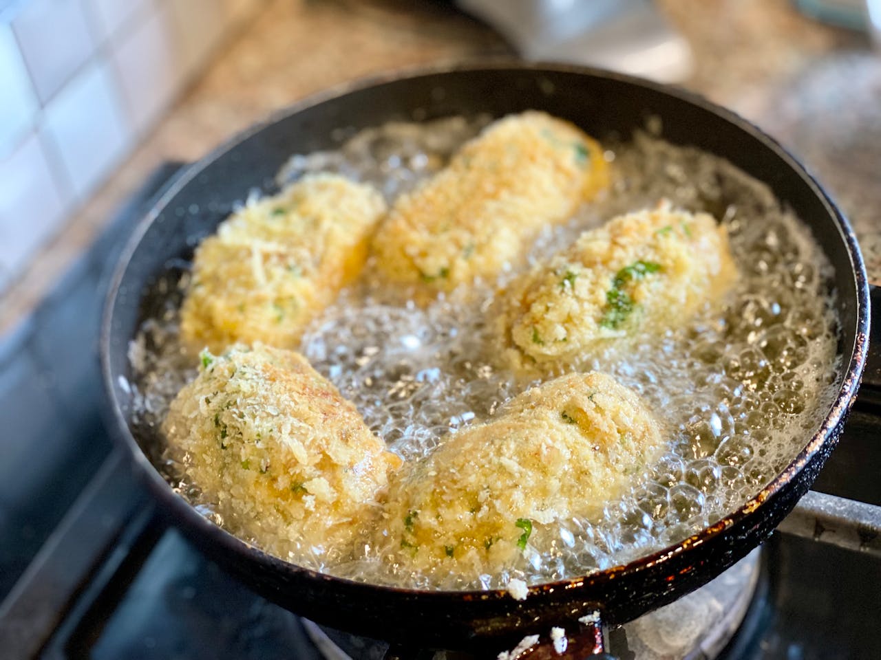 Close-up of golden croquettes frying in a pan with bubbling oil, showcasing texture.